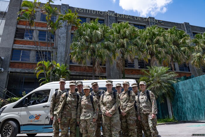 A group of U.S. service members stands in front of a building titled "INSTITUTO NACIONAL DE SALUD"