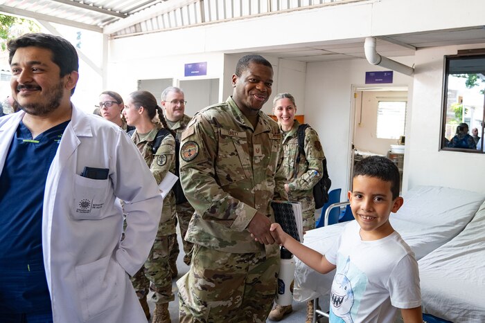 A U.S. servicemember shakes the hand of a child in a hospital.