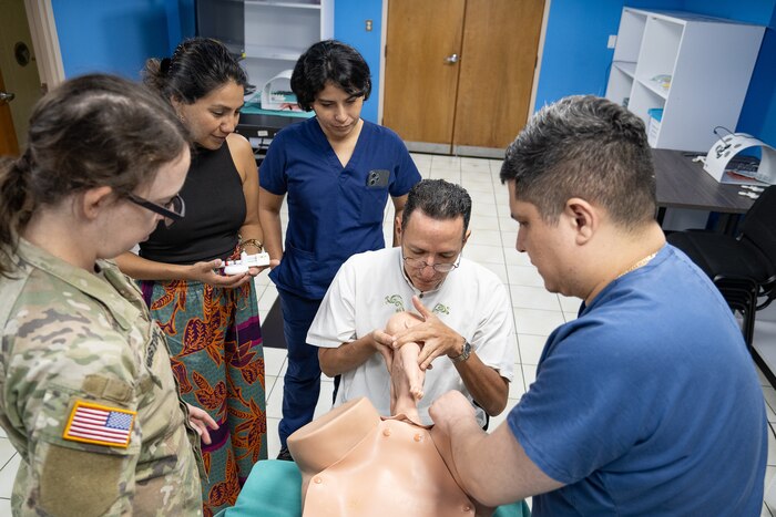 A man pulls a child training mannequin out of another mannequin while onlookers observe.