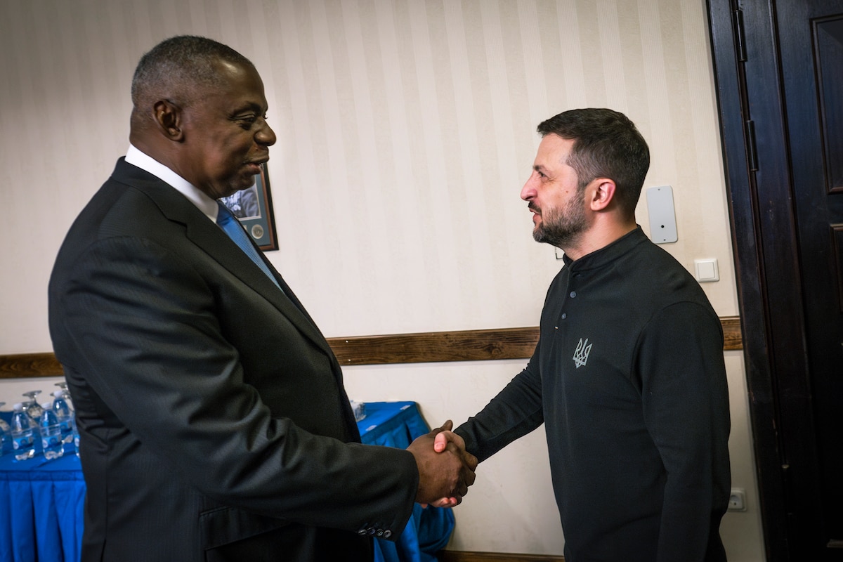 A man in a business suit and a man in a sweater are shaking hands.