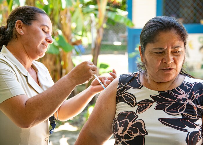A woman injects a shot into the arm of a second woman.
