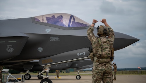 An airman signals a jet to park on the flightline