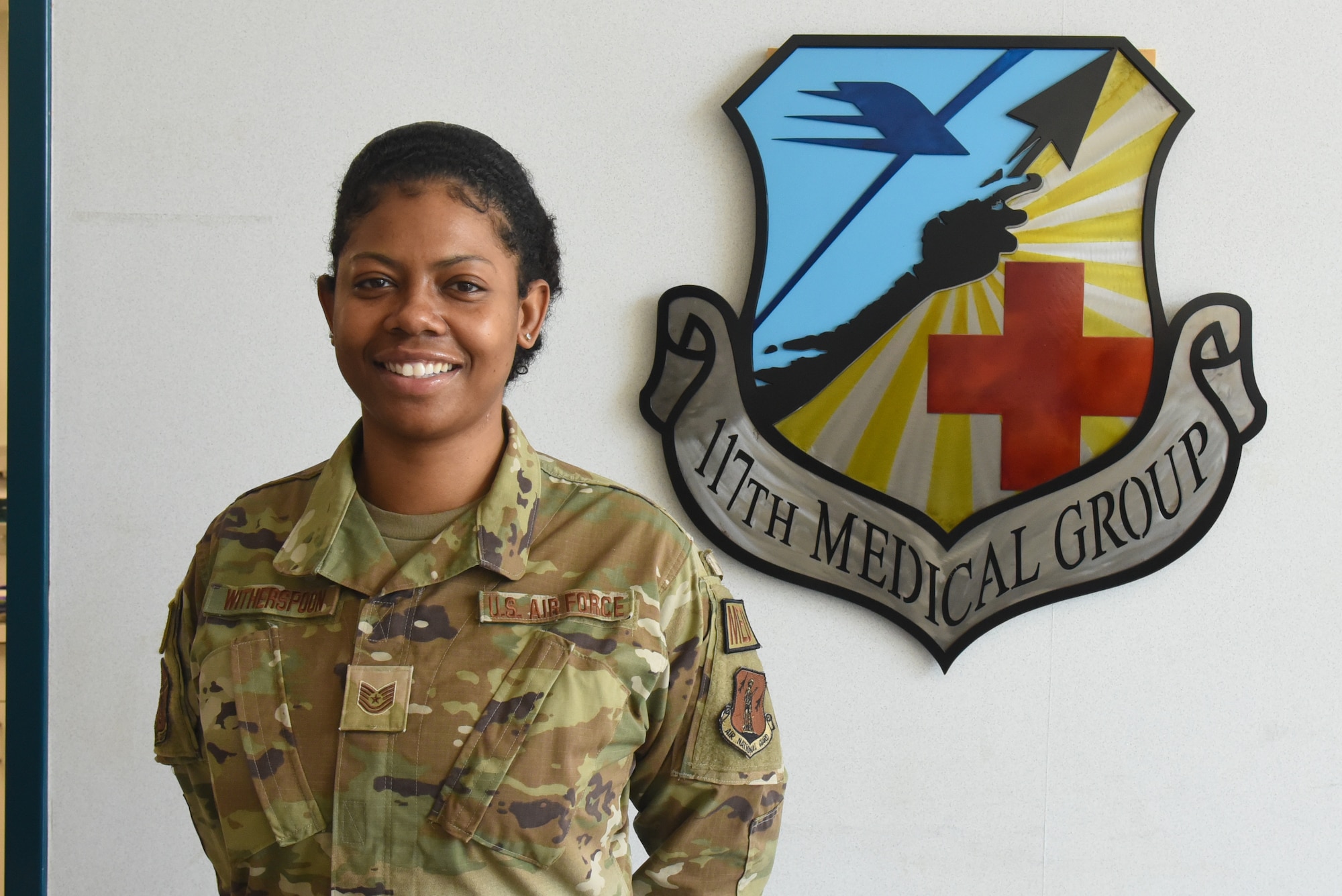 Tech. Sgt. Witherspoon poses in front of a medical group plaque.
