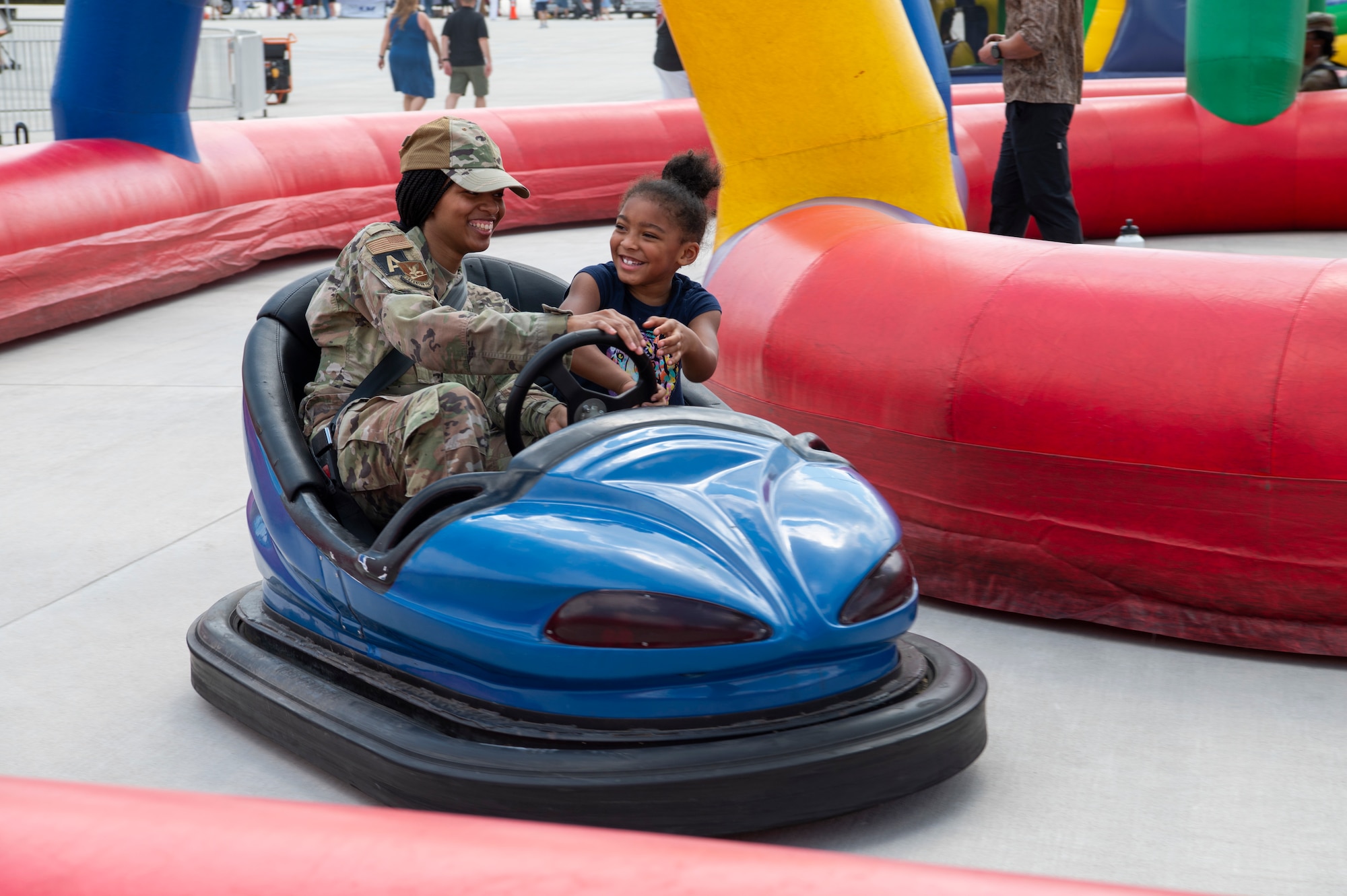 An airman and a child ride a bumper cart together.