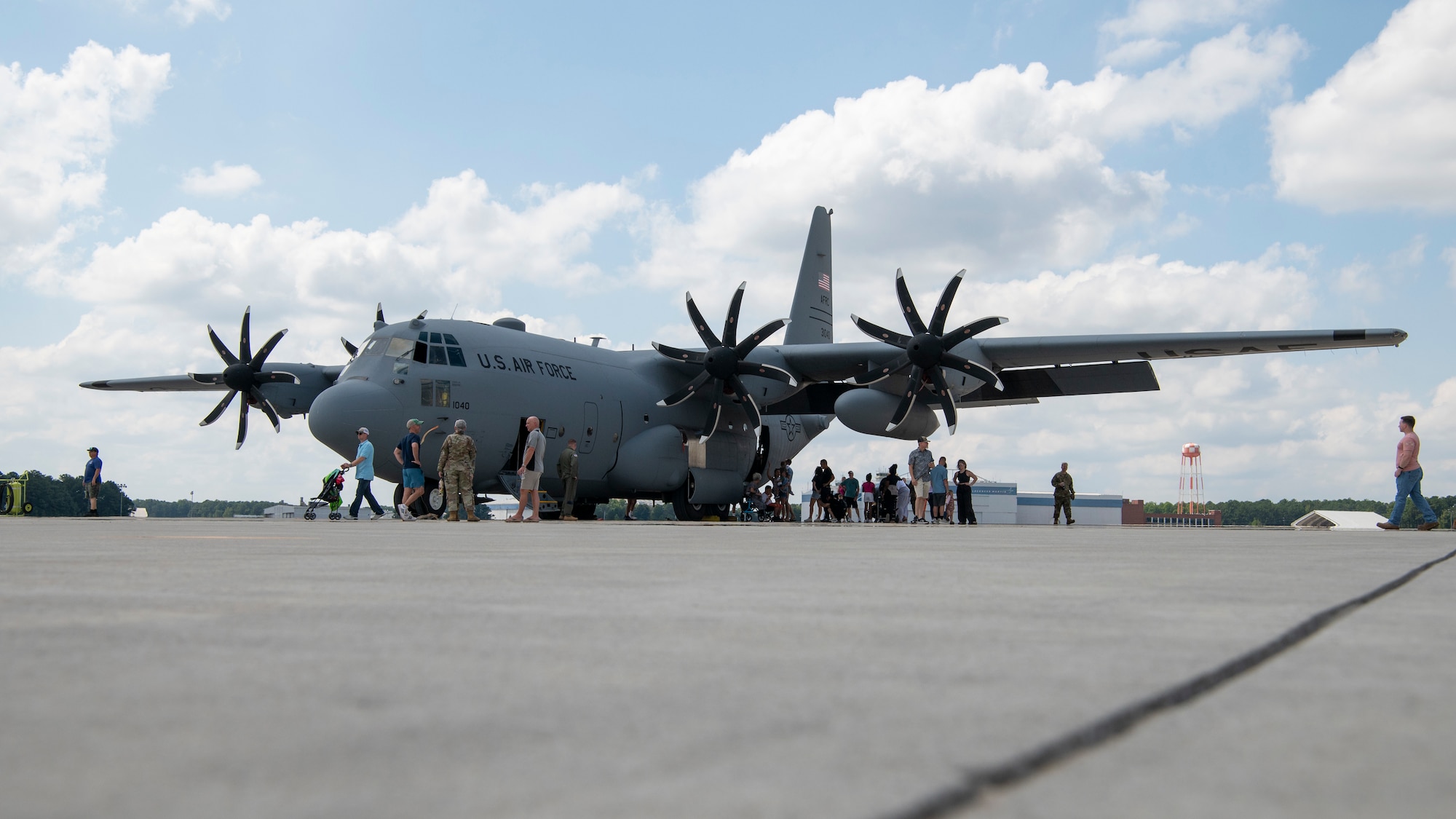 Airmen and their family members line up to take a tour of a C-130 static display out on a flight line.