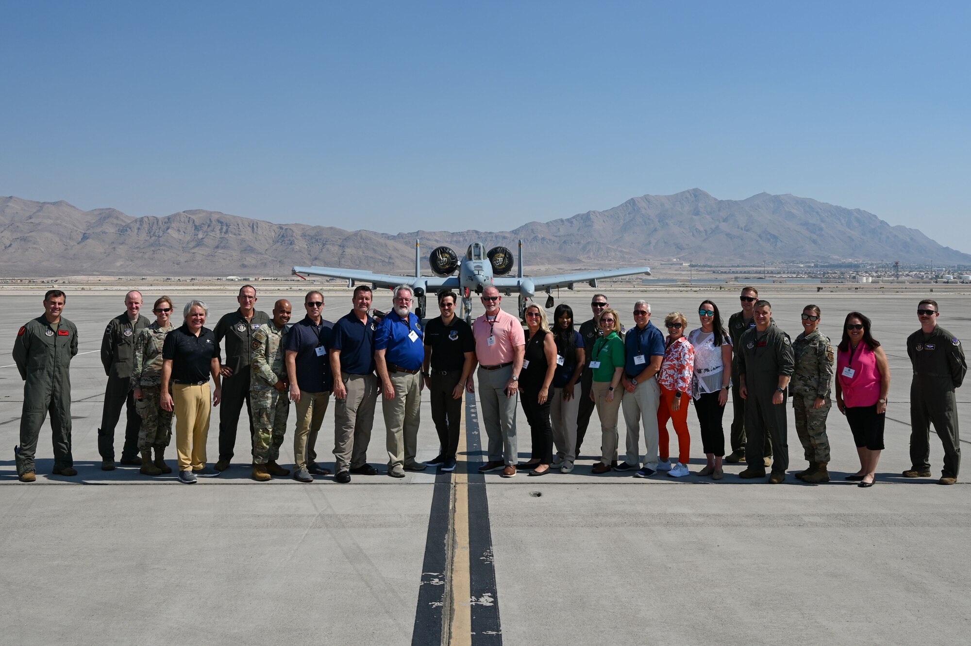 A group of people stand shoulder-to-shoulder in front of an A-10 Warthog displayed on the flight line.