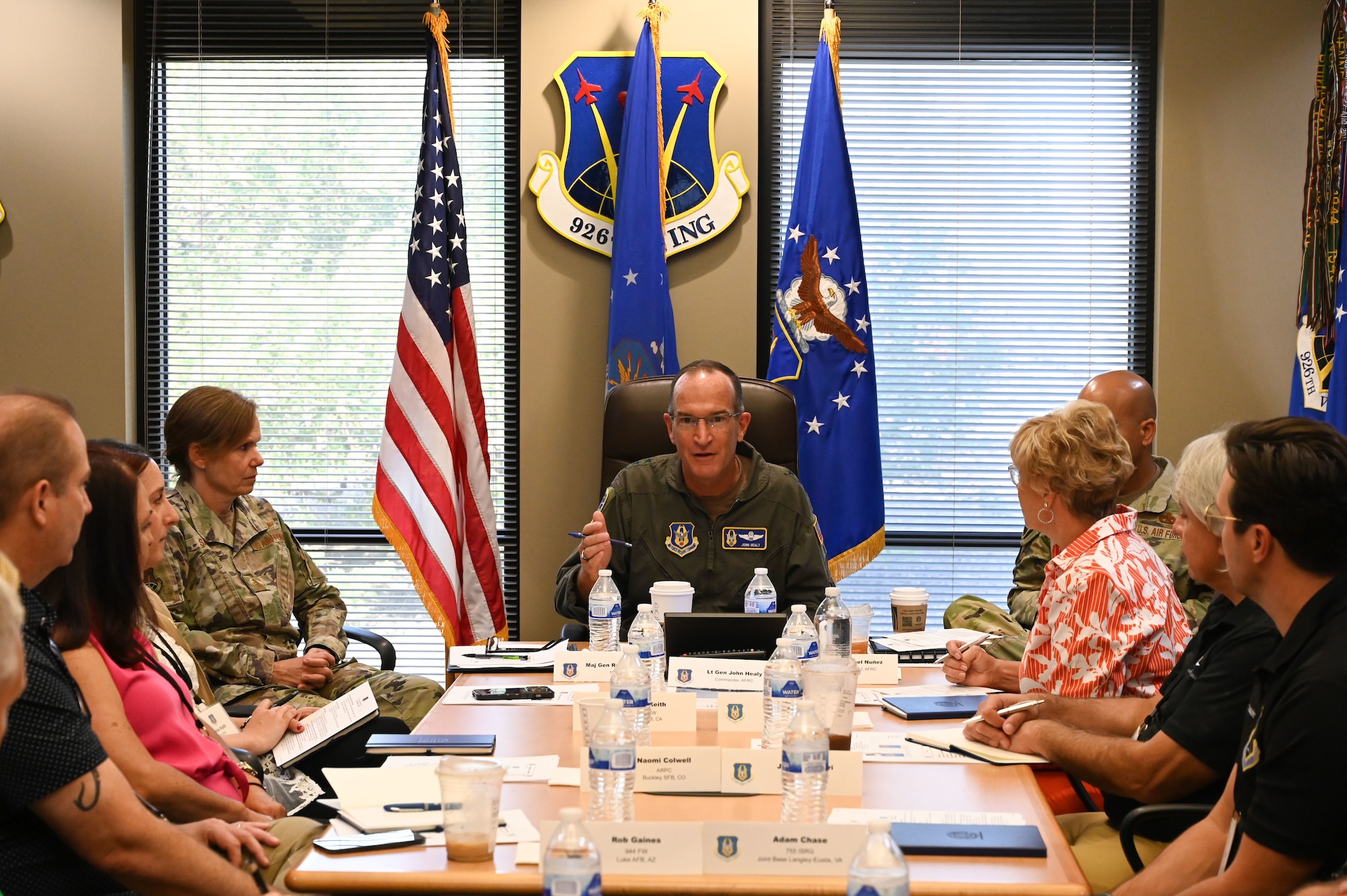 U.S. Air Force Lt. Gen. John Healy speaks while sitting at the head of a conference room table as others seated listen.
