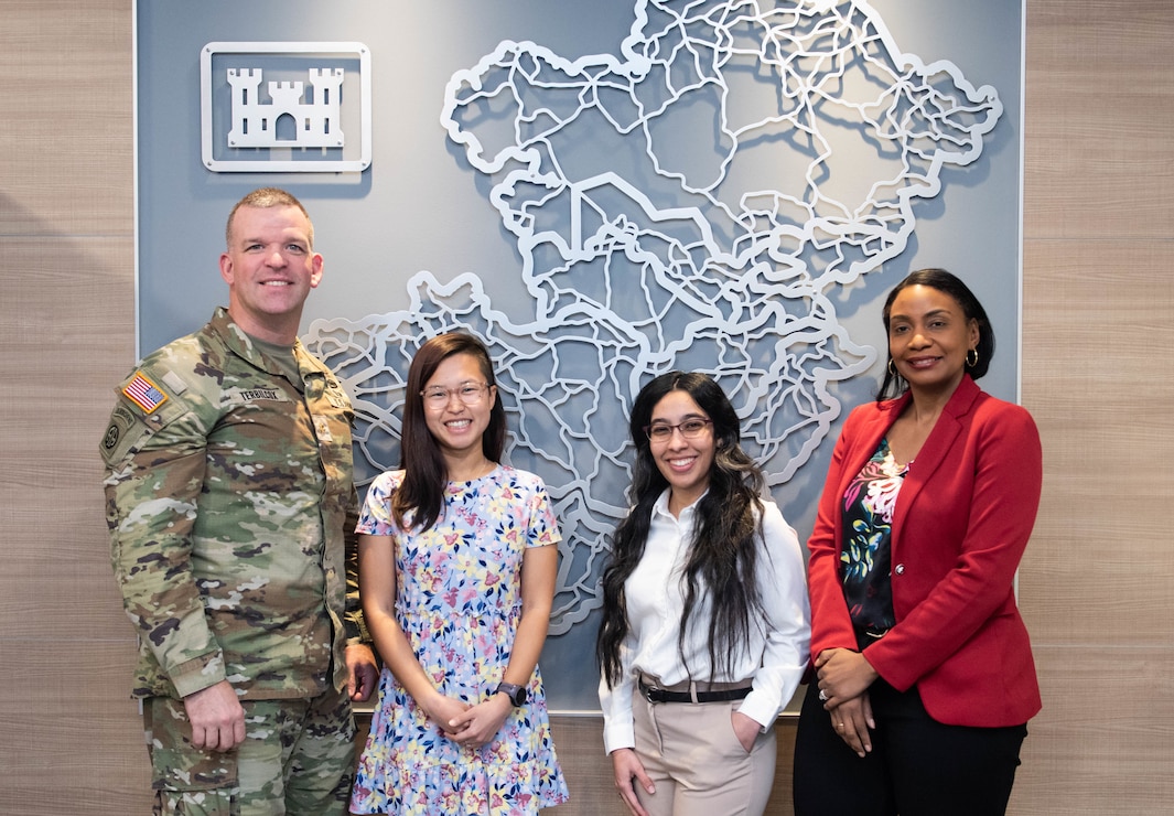 One man in uniform and three women stand in sign of a map of the Middle East.