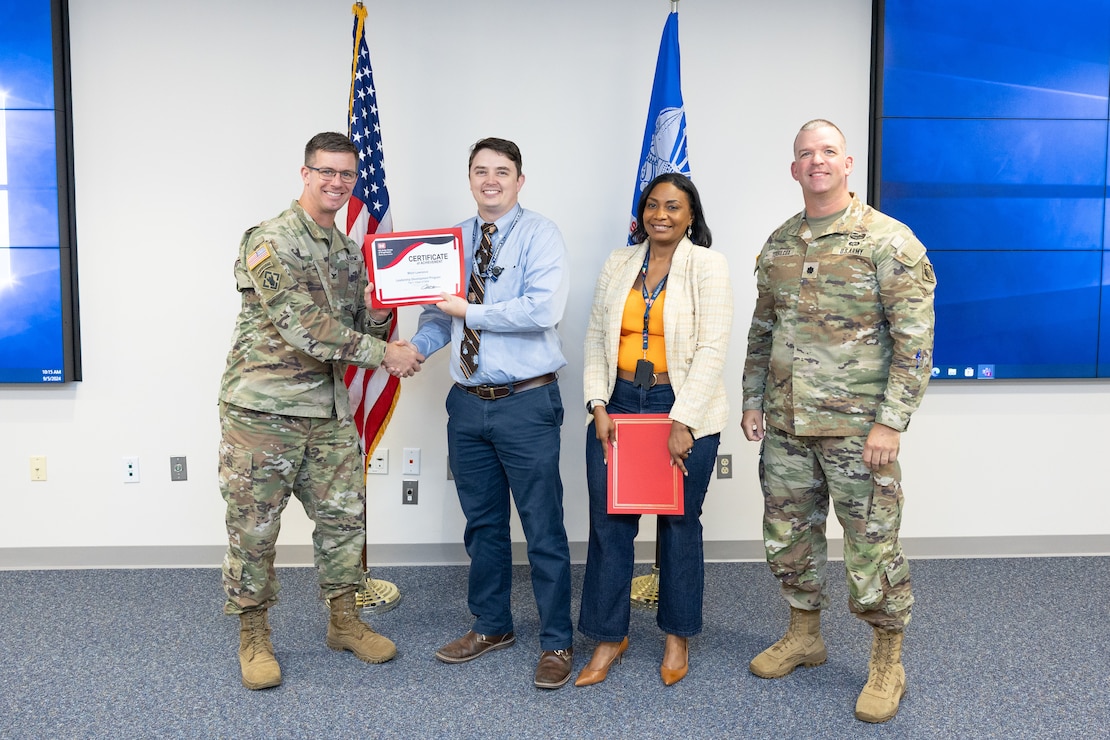 A man in uniform hands another man a certificate while a woman and another man in uniform stand next to them.