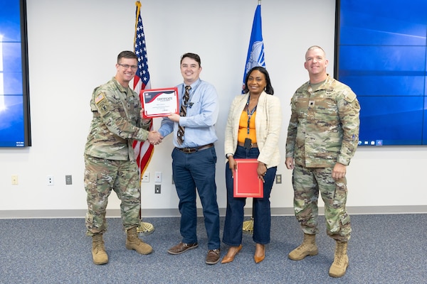 A man in uniform hands another man a certificate while a woman and another man in uniform stand next to them.