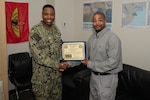 A black man in camo uniform shakes hands with another black man holding a certificate.