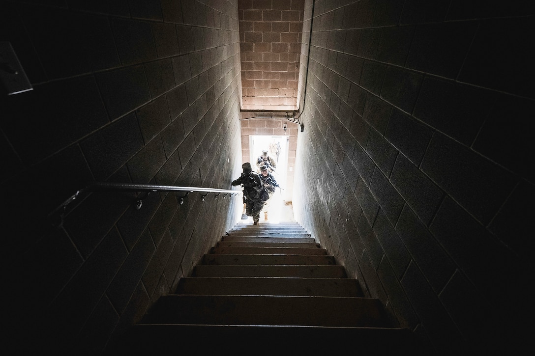 Three airmen walk up a dark stairway while holding weapons.