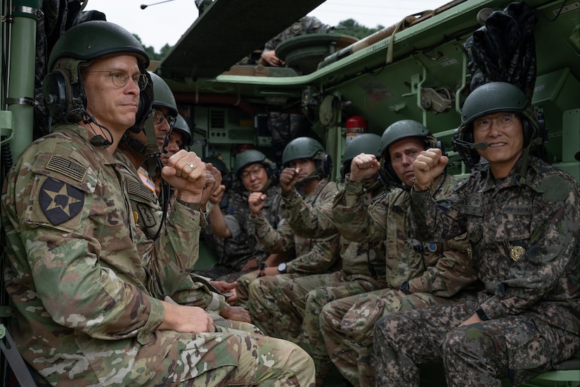 A group of U.S. and South Korean service members wearing helmets sit pose for a photo inside a military vehicle.