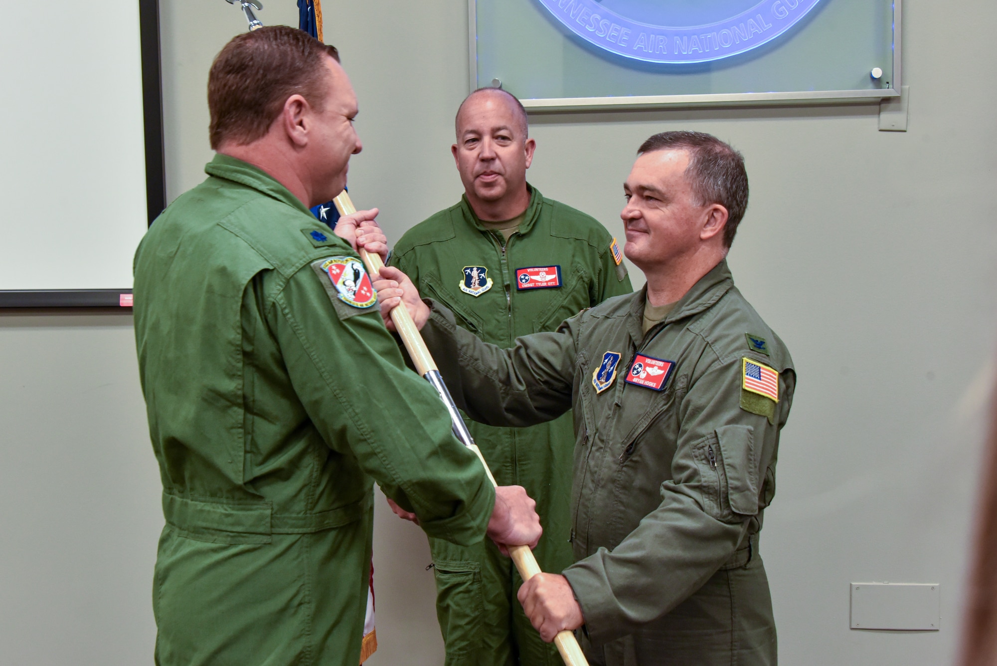 National guardsmen passing the guidon during a change of command ceremony in an indoor setting.