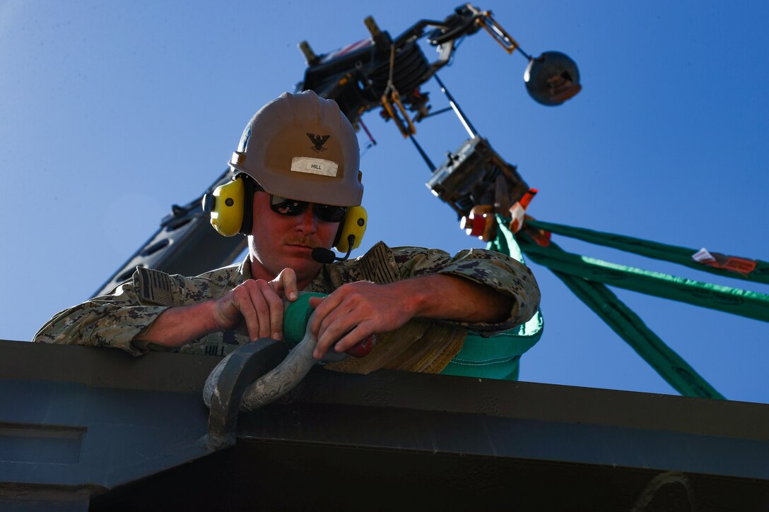 Construction Mechanic 3rd Class Nickolas Hill, assigned to Naval Mobile Construction Battalion (NMCB) 4 detaches straps from a rock hopper after it was lifted by a crane to assemble a mobile rock breaker on August 19, 2024, at Naval Base Ventura County, Port Hueneme, California.