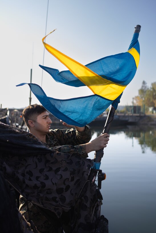U.S. Marine Corps Lance Cpl. Nicholas Guarino, small arms repairer, puts the Swedish flag on the stern of a CB90 combat boat at Berga Naval Base, Sweden, Aug. 29, 2024. Marines assigned to 4th Assault Amphibian Battalion, 4th Marine Division, Marine Forces Reserve, are deployed for training in support of Exercise Archipelago Endeavor, an annual integrated, Swedish Armed Forces-led exercise that increases operational capabilities between U.S. Marines and Swedish forces. (U.S. Marine Corps photo by Sgt. Scott Jenkins)