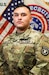 U.S. Army Soldier in uniform poses in front of American Flag and USAREC Flag for official headshot