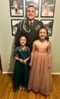 Soldier in dress uniform poses with two young girls in formal dresses