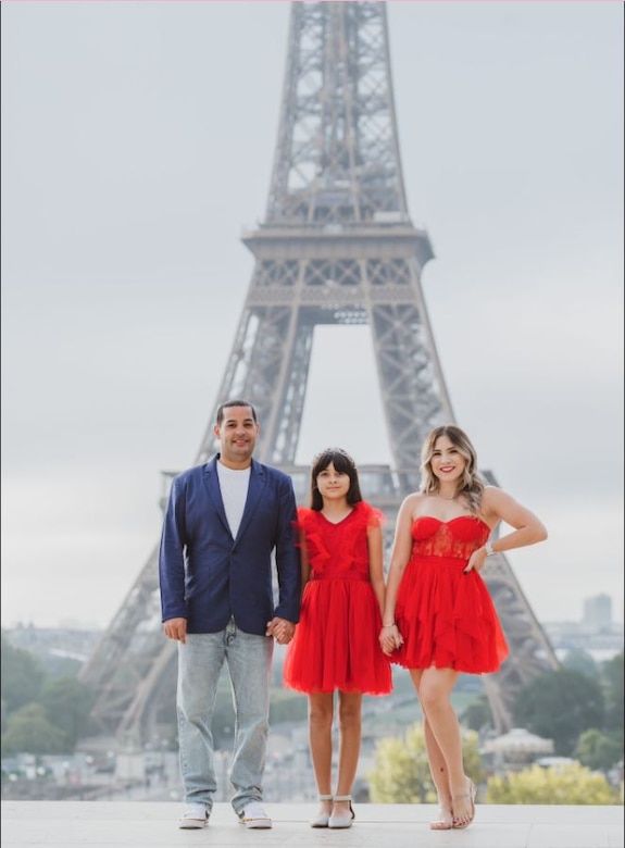 Family consisting of a father, mother and daughter poses together in front of the Eiffle Tower