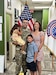 U.S. Army Soldier in uniform poses with wife, son and daughter in front of an American Flag and a USAREC Flag.