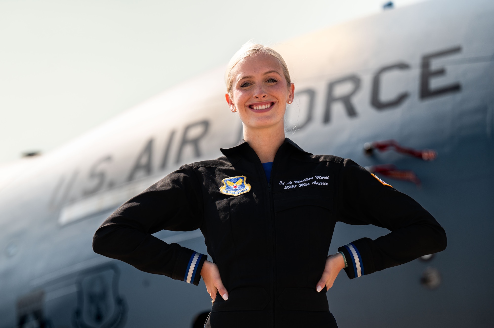 woman in flight suit poses in front of large grey aircraft with "U.S. Air Force" painted on its side