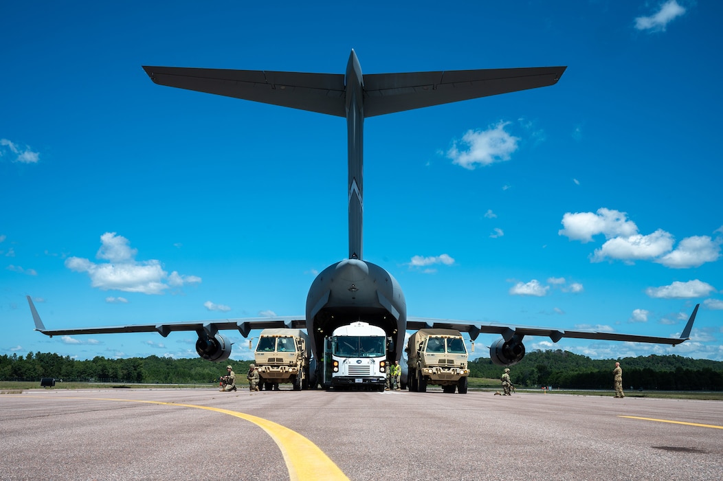 A convoy of Light Medium Tactical Vehicles and a mass-casualty medical transport bus line up against a 445th Airlift Wing C-17 Globemaster III for patient transfer during Exercise Patriot Medic 2024 at Fort McCoy Army Airfield, Wisconsin, August 11, 2024. Patriot Medic leveraged specialized training opportunities and partnerships with other military branches and allies to develop combat-ready medics. (U.S. Air Force photo by Tech. Sgt. Timothy Leddick)