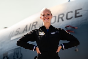 woman in flight suit poses in front of large grey aircraft with "U.S. Air Force" painted on its side