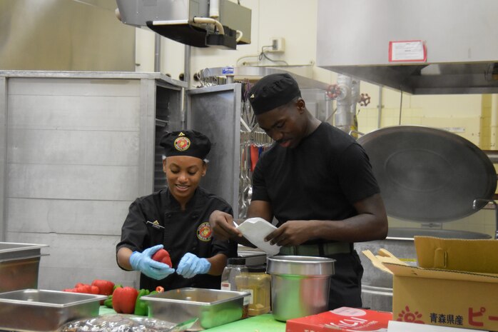 Lance Cpls. Judy Dumas and Kevaughn Bernard, food service specialists assigned to Marine Corps Air Station Futemna prepare food.