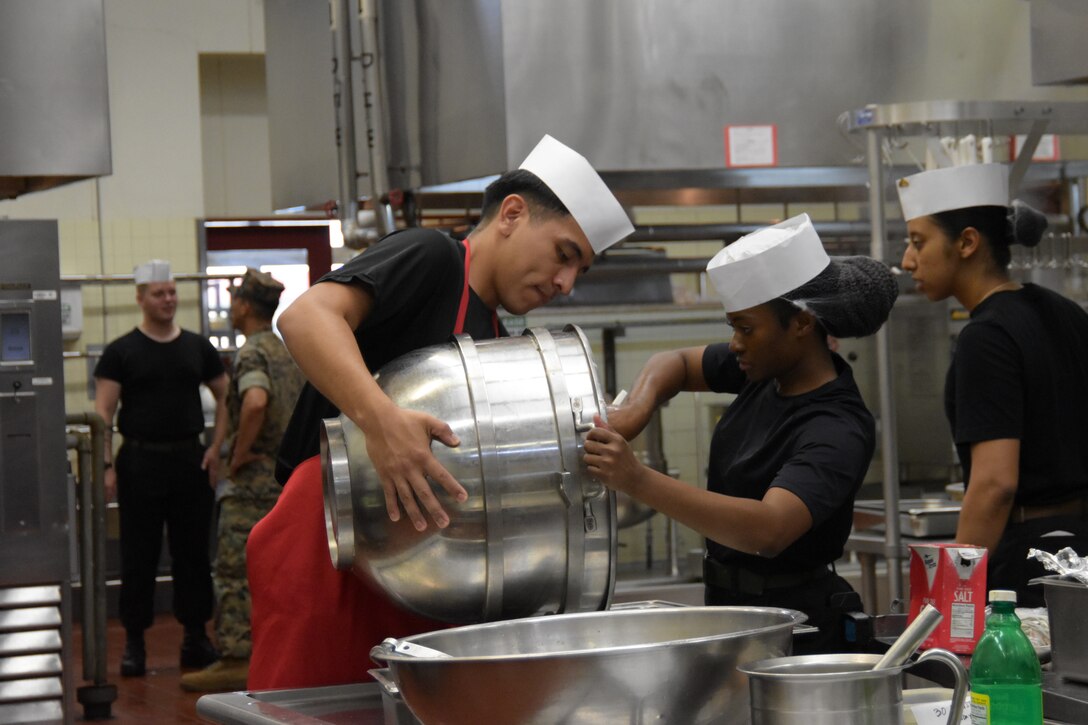 Lance Cpl. Alexis Martinez Nulasco, assigned to Camp Schwab, holds a mixing bowl for Lance Cpl. Judy Dumas, stationed at Camp Kinser, during the Marine Corps Installations Pacific’s Food Services Specialist of the Quarter competition, held at Combined Arms Training Center, Camp Fuji, August 30, 2024.  (U.S. Marine Corps photo by Song Jordan)