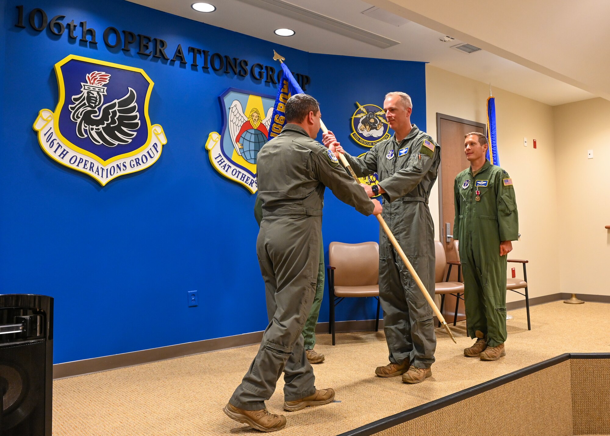 U.S. Air Force Lt. Col. Kyle Hruz, pictured in middle, a 102nd Rescue Squadron HC-130J Combat King II pilot, receives the 102nd Rescue Squadron guidon from U.S. Air Force Col. Jefferey Cannet, 106th Operations Group commander, during a Change of Command ceremony held at the New York Air National Guard's 106th Rescue Wing, F.S. Gabreski Air National Guard Base, Westhampton Beach, NY, June 7, 2024. Hruz assumed command of the 102nd Rescue Squadron, replacing Col. Sean Garell, pictured right, who assumes the role of Deputy Commander of the 106th Operations Group. (U.S. Air National Guard photo by Tech Sgt. Daniel H. Farrell)