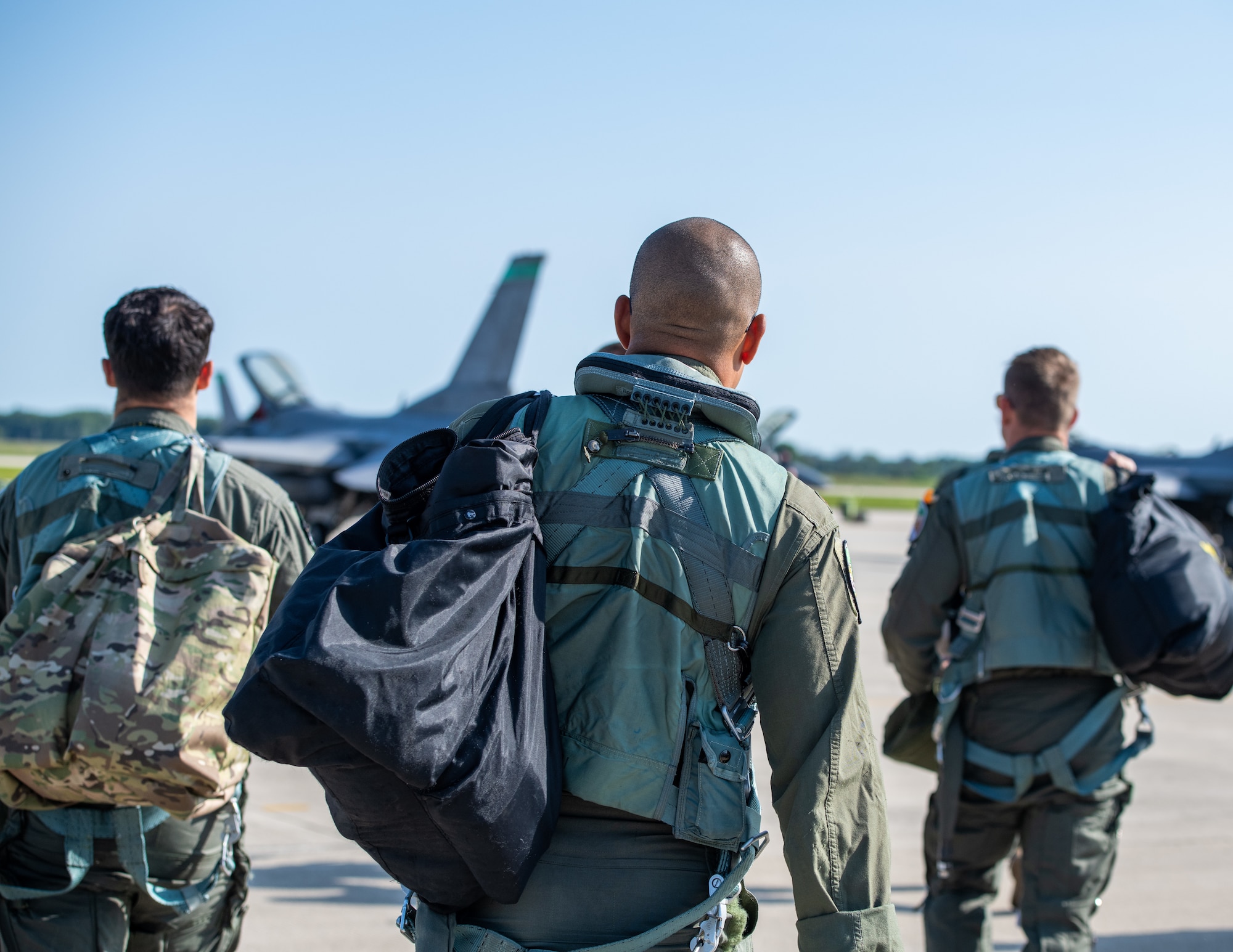 Three fighter pilots walk toward the flight line