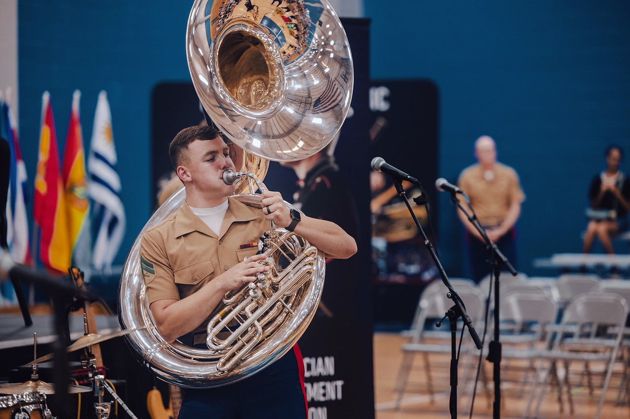 A Marine plays tuba in a hall with people in the background.