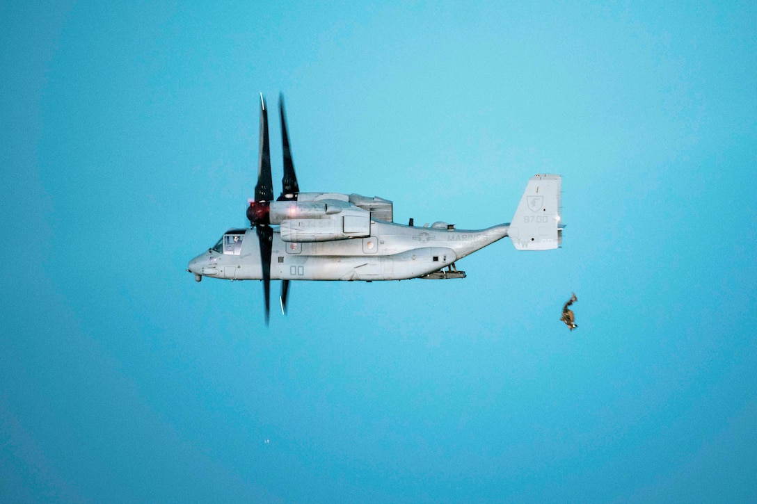 A Marine free falls behind an aircraft in a bright blue sky.