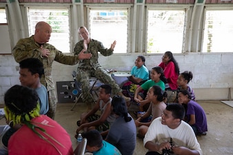 Lt. j.g. Katelyn Tebou, center, dances as Royal Australian Air Force Wing Cmdr. Scott Minchin, left, sings to students at Colonia Middle School in Yap, Federated States of Micronesia.