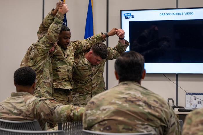 Three men stand in a row with the middle man in motion having his arms put around the others' shoulders