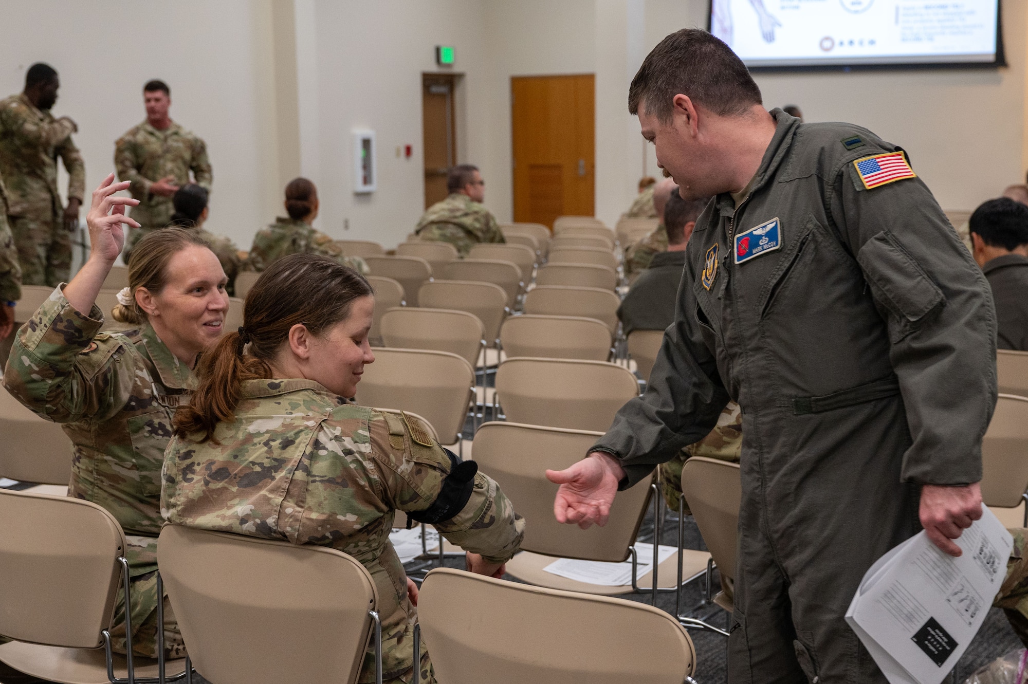 1st Lt. Mccoy looks over at two Airmen seated, one raising her hand and the other gesturing to her tourniquet