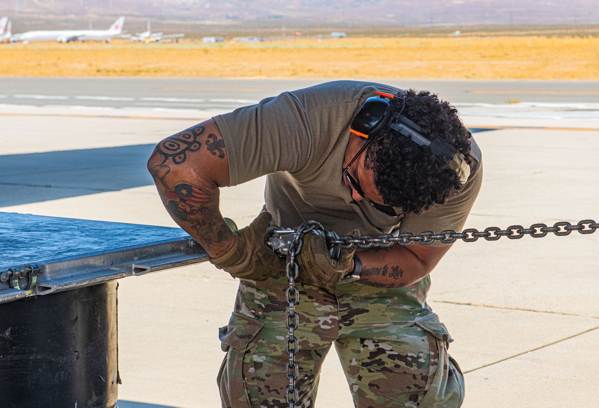 U.S. Air Force Senior Airman Victor Colas, 621st Contingency Response Squadron crew member, tightens chains on a metal pallet for a combat offload operation during exercise Agile Flag 24-3 at Mojave, California, Aug. 8, 2024. The operation was a demonstration of the squadron's ability to quickly offload cargo using commonly found airfield items. During AGILE FLAG 24-3, the 23rd Wing provided the Air Expeditionary Wing leadership element, the Command and Control Force Element, and the Air Base Squadron at two separate locations exercising rapid insertion into theaters, establishing logistics and communications with theater C2, receipt of follow-on forces, mission generation, and combat power projection across all domains, while making critical decisions needed to remain agile. (U.S. Air Force photo by Airman 1st Class Sir Wyrick)