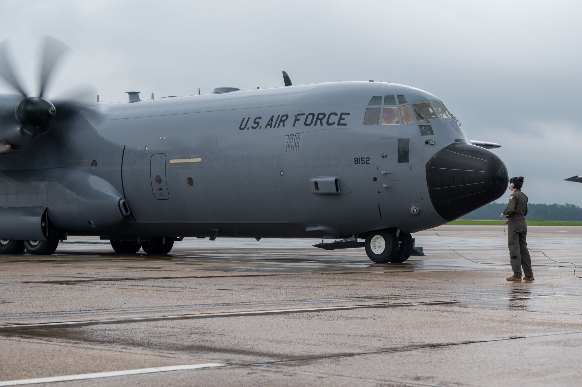 A loadmaster stands and watches a C-130J start up