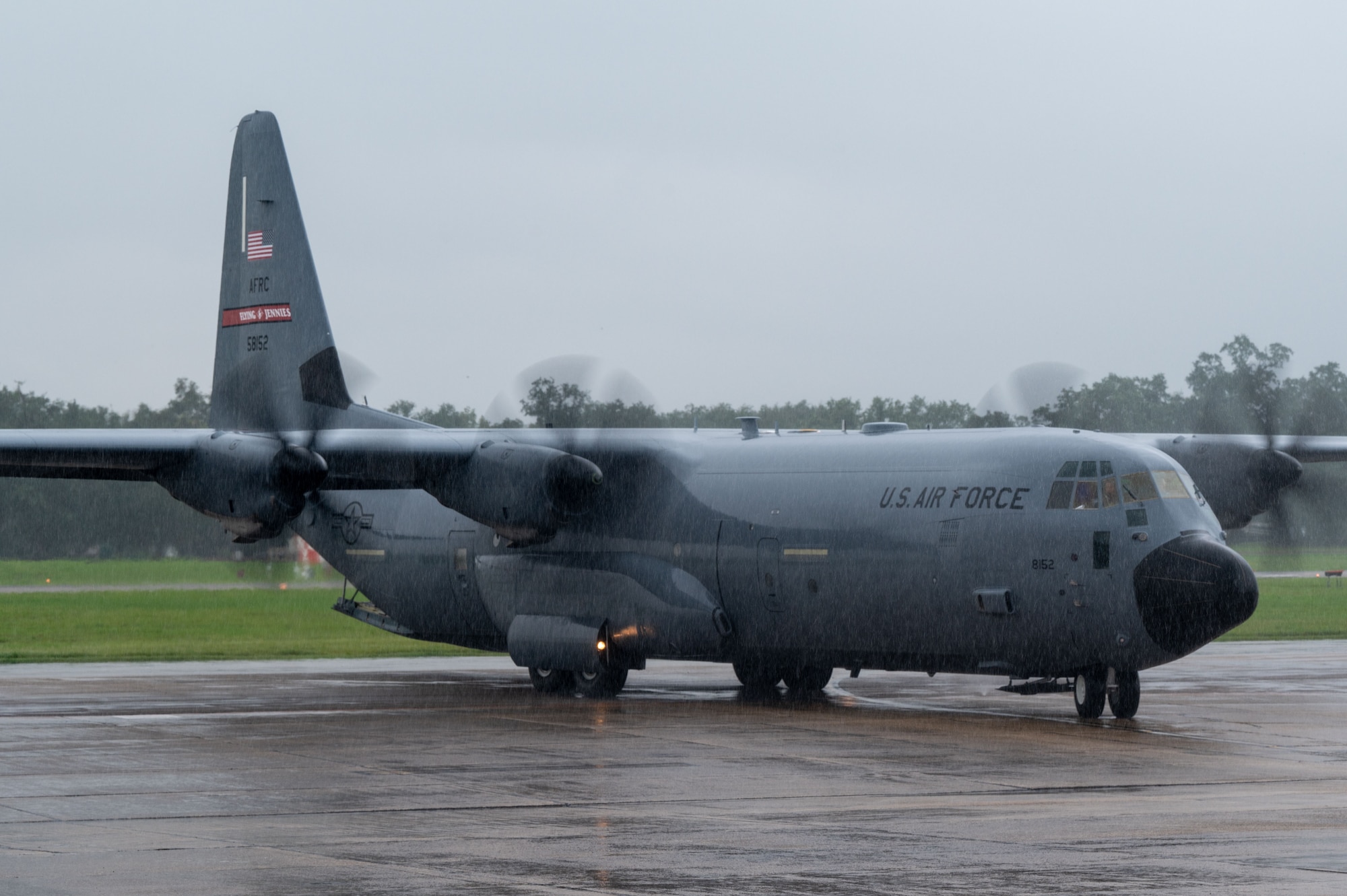 A C-130J backs from it's parking spot. It is raining heavily.