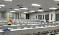 worker walks through rows of installed desks and chairs in a large classroom.