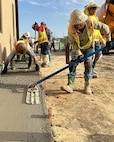 worker pushes a float over fresh concrete while others behind him smooth out rough spots with a trowel.