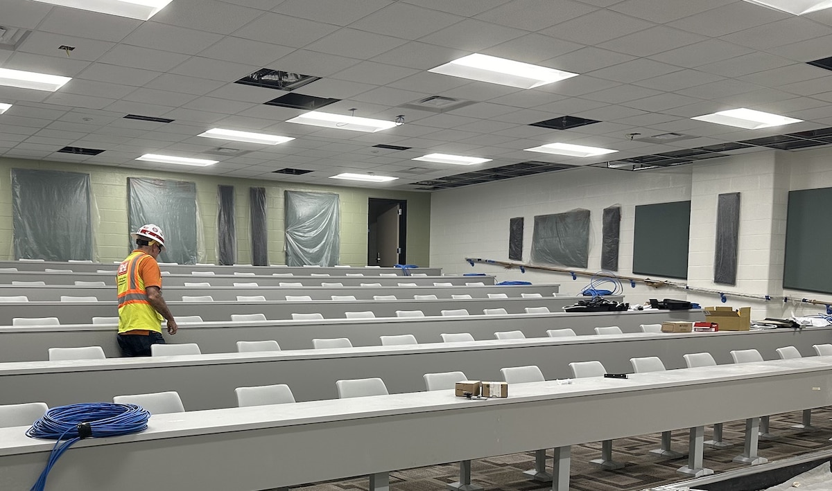 worker walks through rows of installed desks and chairs in a large classroom.