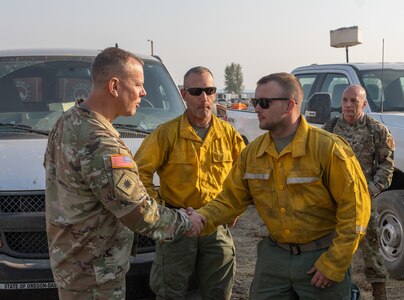 Brig. Gen. Alan R. Gronewold, the adjutant general of Oregon, presents a challenge coin to Spc. Rodney Chamberlain, an Oregon Army National Guard hand crew member, for exceptional performance fighting the Telephone Fire, Aug. 6, 2024, at the Harney County Fairgrounds fire camp.