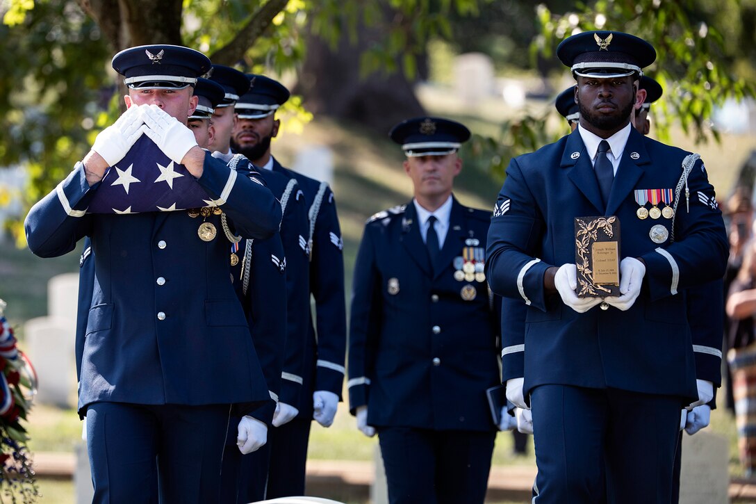 A group of airmen in an honor guard stand at attention in a cemetery.