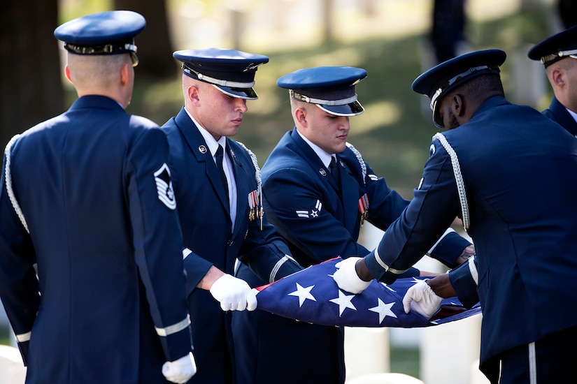 A group of airmen fold the U.S. flag while one stands at attention.