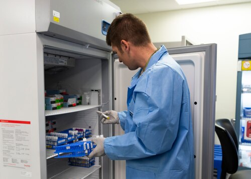 Medical technician places laboratory samples in refrigerator.