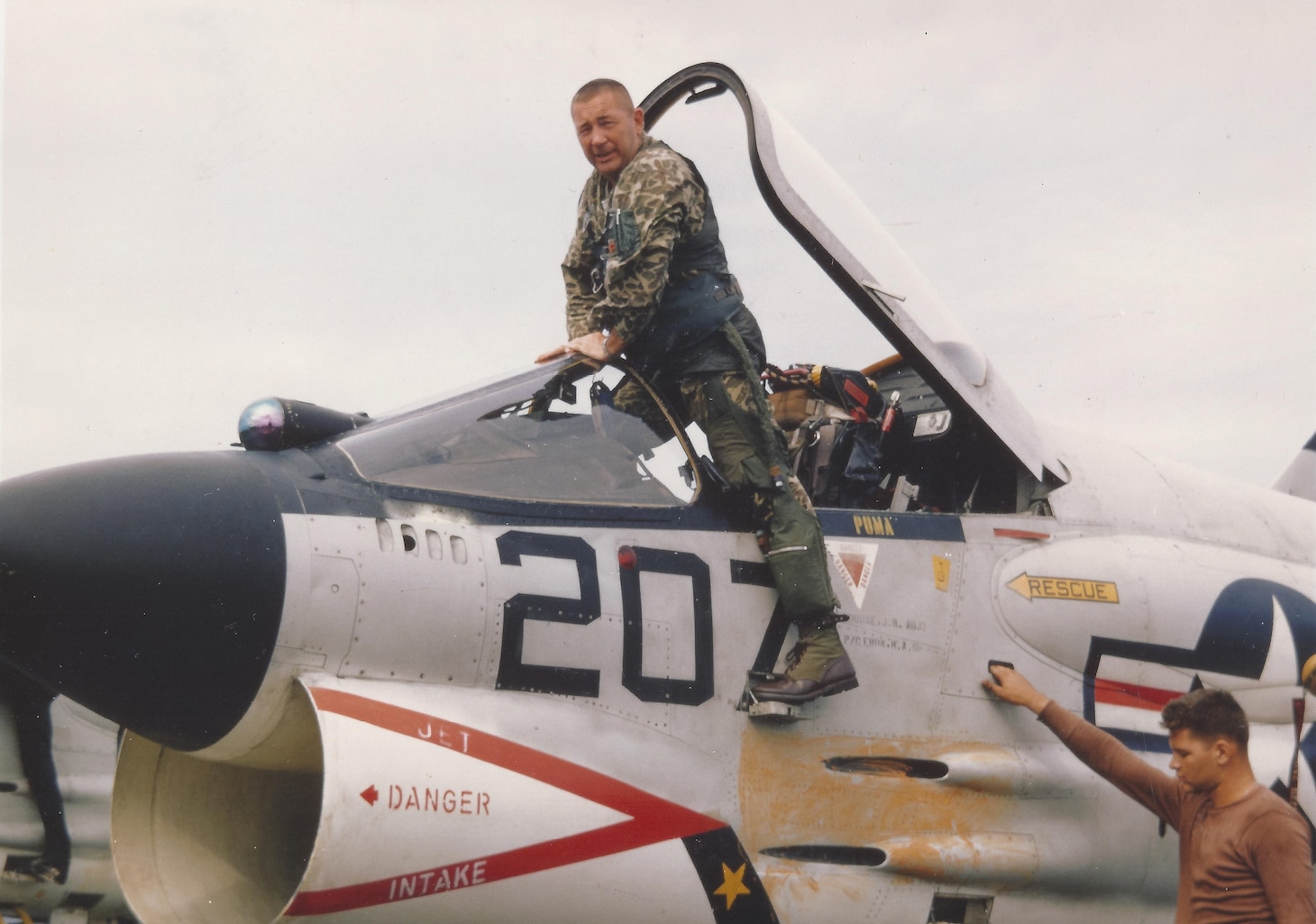 Fighter Squadron (VF) 162 commanding officer Cmdr. Dick Bellinger gets out of F-8E AH 207 following a mission from the Oriskany (CVA 34). Instead of the Navy-supplied flight suit, he sports the so-called camouflaged “duck hunter” suit the squadron obtained before the cruise from a sporting goods store near their base.  Not being made of fire-retardant NOMEX, it was not the official flight suit the Navy supplied all flight crews