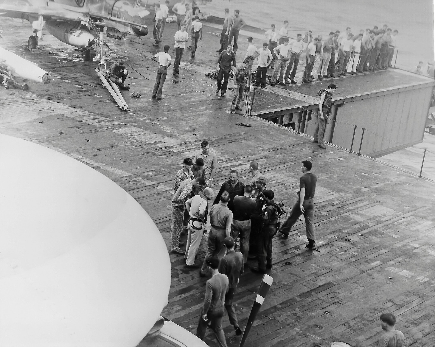 On Oct. 26, 1966, the Oriskany dealt with a tragic fire that resulted in 44 killed and injured 156, many from its Air Wing 16 crews. Like several of his friends and fellow aviators, Bellinger was caught below deck but finally made his way to the safety of the flight deck. In the center of the group, surrounded by friends and shipmates, Bellinger is in a Navy flight suit, they all take stock of who is there, and who isn’t.