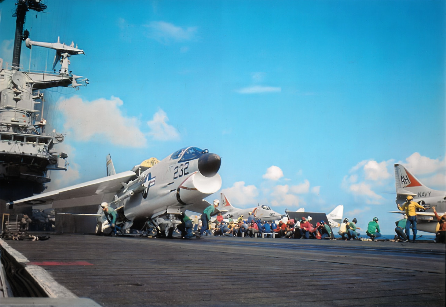 Fully armed with Sidewinder air-to-air missiles, a VF-162 F-8E and its pilot get last-minute attention from flight-deck crewmen before launching from the Oriskany. A VA-164 A-4E marked by its distinctive orange tail chevron is in the background.