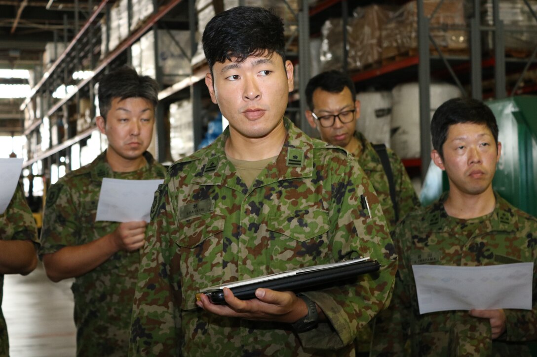 Japanese Ground Self Defense Force officers in a warehouse listen to a briefing.
